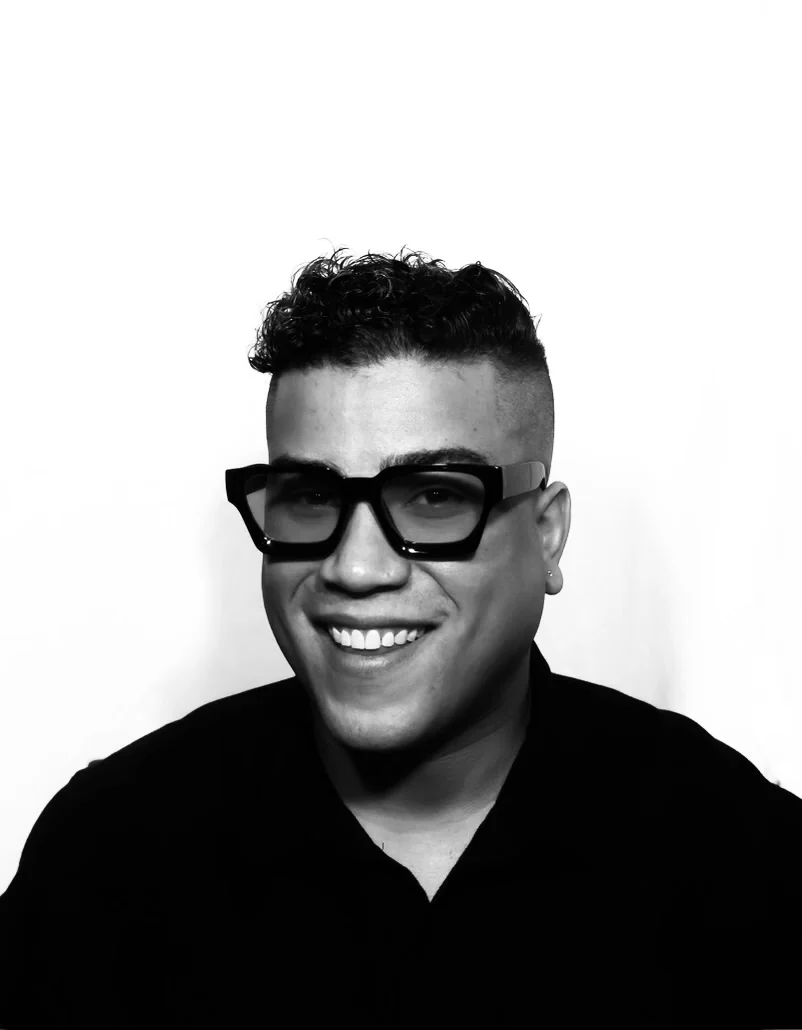 Sacha John Bissonnette, smiling, in black-framed glasses and a black shirt